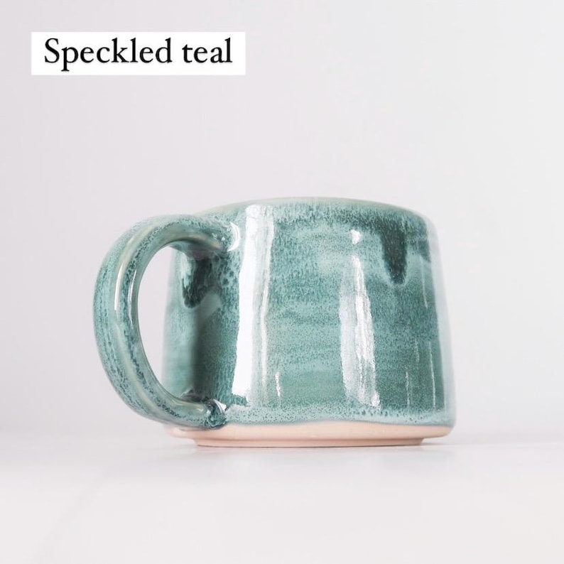 May include: A speckled teal ceramic mug with a rounded handle. The mug has a light pink rim.