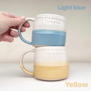 May include: Two ceramic mugs, one light blue and one yellow, stacked on top of each other. Each mug has a white upper section and a colored lower section. The text "HAPPY 8TH ANNIVERSARY 11.03.2023" is inscribed on each mug.