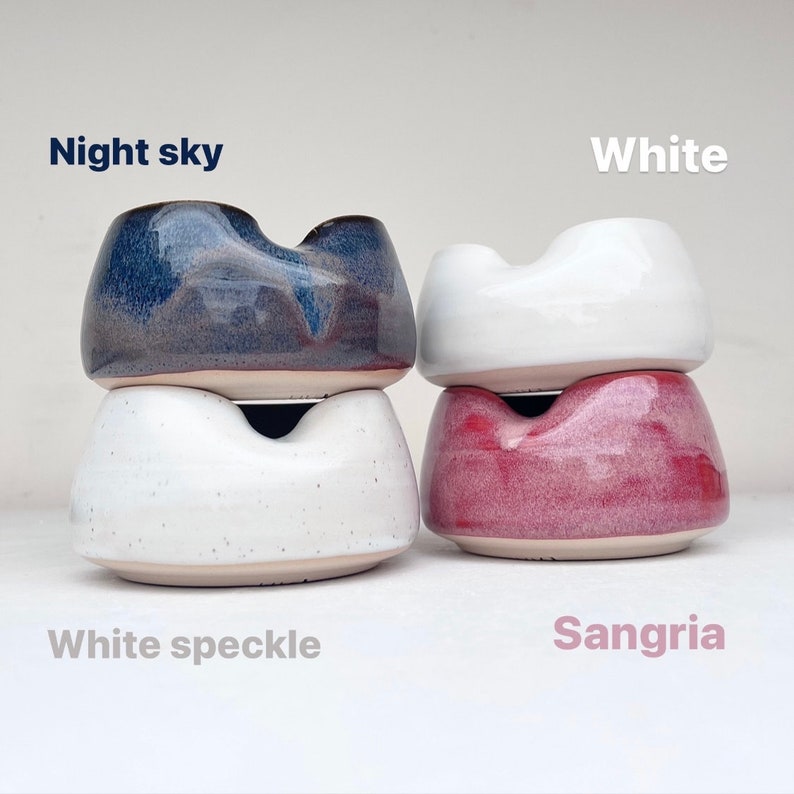 May include: Three ceramic bowls stacked in pairs. The top bowl is a dark blue with a purple hue, labeled "Night sky". The middle bowl is white with speckles, labeled "White speckle". The bottom bowl is a light pink with a white hue, labeled "Sangria". The rightmost bowl is white, labeled "White".