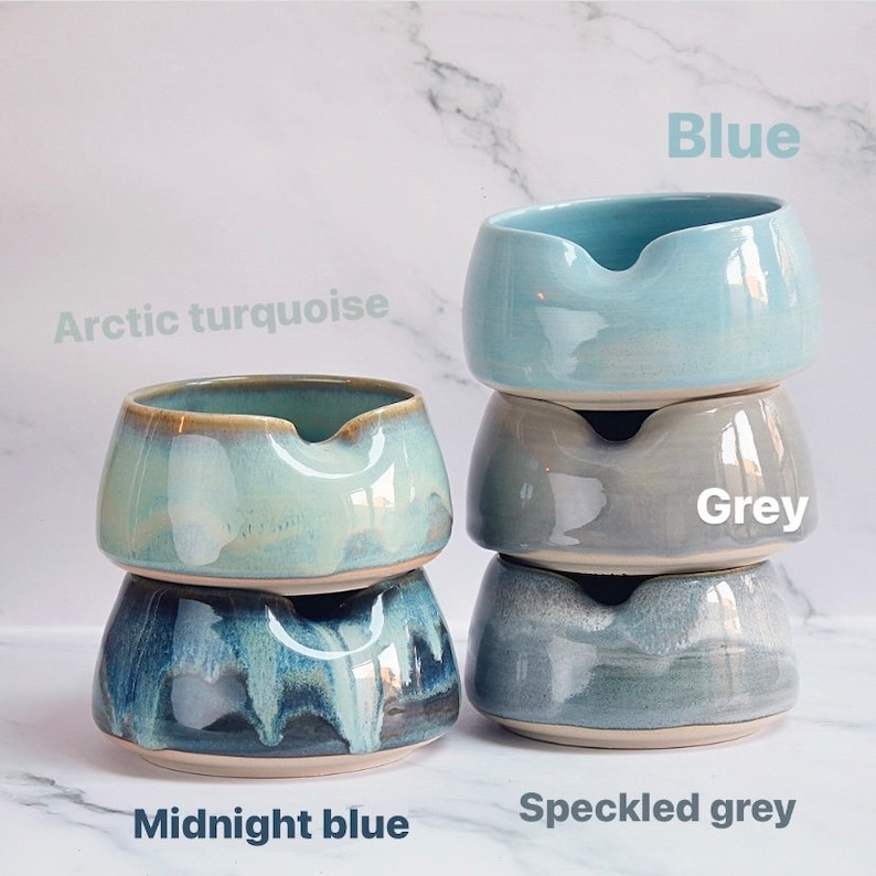 May include: Four ceramic bowls in various shades of blue and grey. The bowls are stacked in pairs, with the top bowl of each pair being a lighter shade than the bottom bowl. The bowls are labeled "Arctic turquoise", "Midnight blue", "Blue", "Grey", and "Speckled grey".