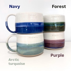 May include: Four ceramic mugs stacked together, each with a unique color band. The colors include navy, forest green, arctic turquoise, and purple. Each mug has a white upper section and a handle. Names are etched on the mugs.