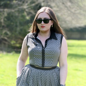 Puede incluir: Una mujer con un vestido estampado en blanco y negro con un cinturón negro. Lleva gafas de sol y tiene el pelo recogido hacia atrás.