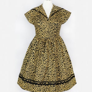 Puede incluir: Un vestido de estampado de leopardo amarillo y negro con manga corta y cuello. El vestido tiene un ribete de encaje negro alrededor del dobladillo.