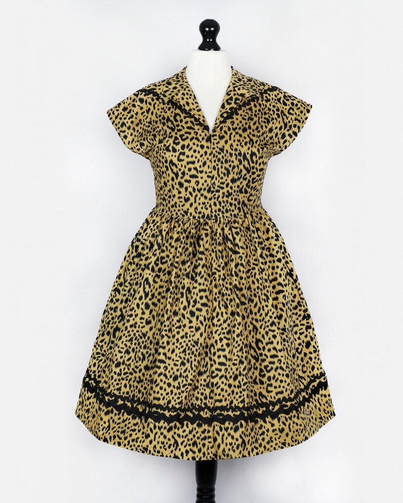 Puede incluir: Un vestido de estampado de leopardo amarillo y negro con manga corta y cuello. El vestido tiene un ribete de encaje negro alrededor del dobladillo.