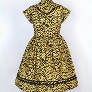 Puede incluir: Un vestido de estampado de leopardo amarillo y negro con mangas cortas y un ribete de encaje negro alrededor del cuello y el dobladillo.