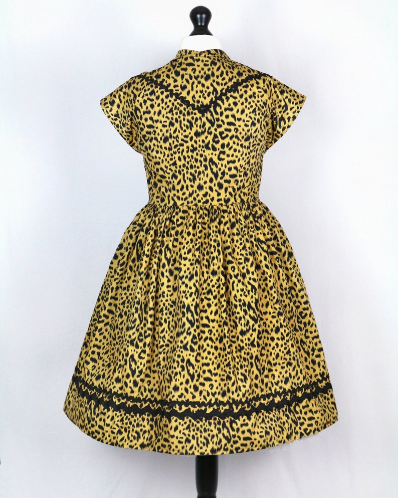 Puede incluir: Un vestido de estampado de leopardo amarillo y negro con mangas cortas y un ribete de encaje negro alrededor del cuello y el dobladillo.