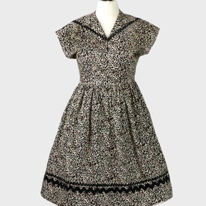 Puede incluir: Un vestido vintage con estampado de leopardo y ribete negro. El vestido tiene un corpi&ntilde;o ajustado y una falda completa.