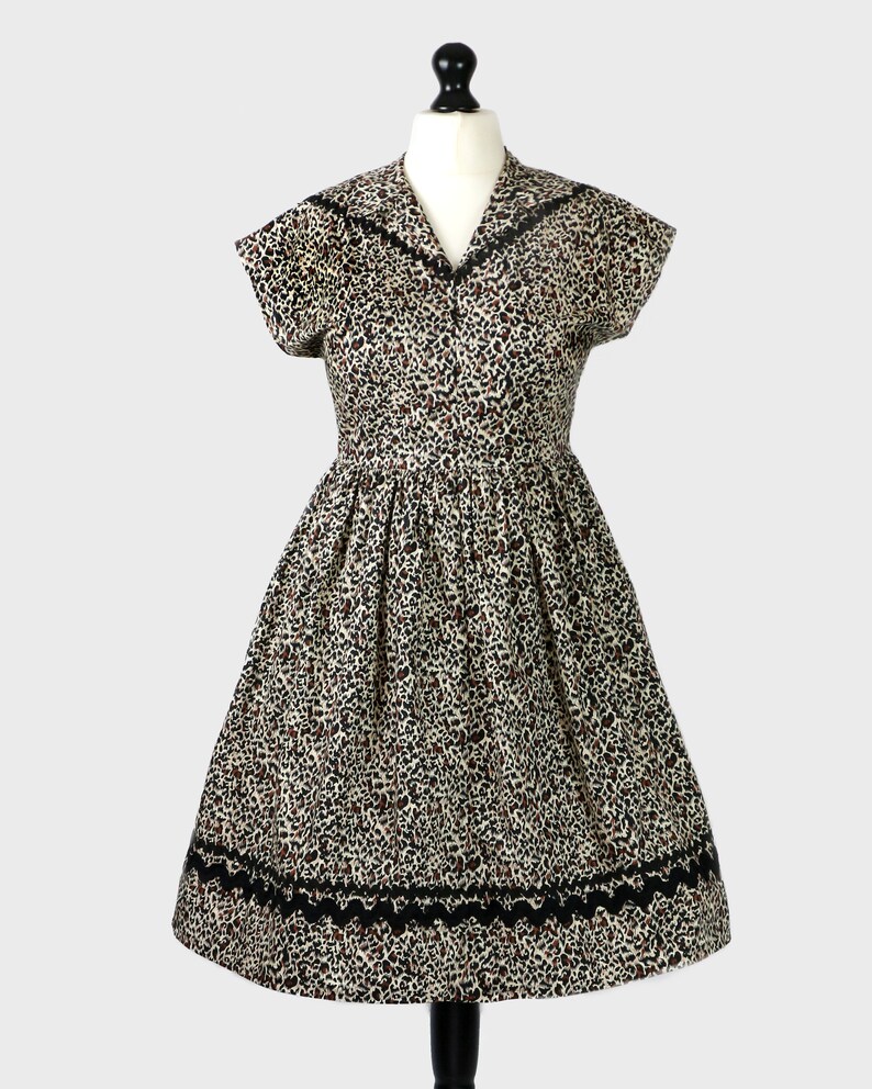 Puede incluir: Un vestido vintage con estampado de leopardo y ribete negro. El vestido tiene un corpi&ntilde;o ajustado y una falda completa.