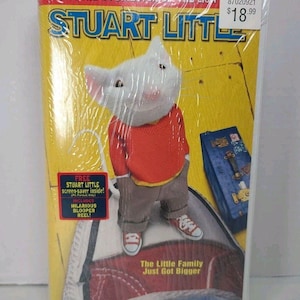Könnte beinhalten: Eine versiegelte DVD des Films "Stuart Little" mit der Hauptfigur, einer Maus in einem roten Oberteil und grauer Hose. Die Verpackung enthält den Text "From the Co-Director of The Lion" und "The Little Family Just Got Bigger."