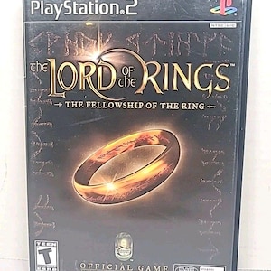 Puede incluir: Caja de juego de PlayStation 2 para "El Señor de los Anillos: La Comunidad del Anillo". La portada presenta el título en dorado, una imagen de un anillo dorado y el logotipo de PlayStation 2. El juego está clasificado "T" para Adolescentes.