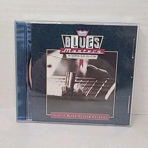 May include: A Blues Masters CD in a clear plastic case. The cover features a close-up of a guitar with a slide, and the text "Blues Masters" and "The Essential Blues Collection". The CD is Volume 15: Slide Guitar Classics.