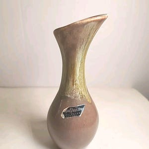 Peut inclure: Un vase en céramique marron avec un dessus évasé et une base bulbeuse. Le vase présente une palette de couleurs bicolores, avec une bande plus claire et texturée près du sommet. Une étiquette est apposée sur le devant du vase.