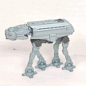 Peut inclure: Un jouet AT-AT de couleur argentée, un véhicule de combat à quatre pattes de la franchise Star Wars. Le jouet présente des éléments mécaniques détaillés, sur fond blanc.
