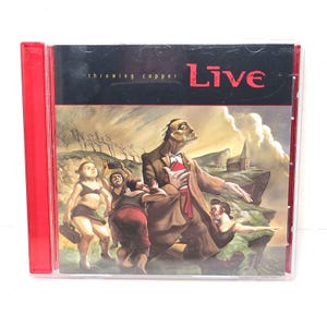 Op de afbeelding: Een cd-hoesje met een rode rug. De cover toont de bandnaam "Live" in het rood en de albumtitel "throwing copper". De illustratie toont figuren op een klif met een kerk op de achtergrond, geschilderd in gedempte tinten.