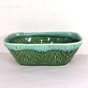 May include: A rectangular ceramic planter with a glossy finish, featuring a deep forest green base and a lighter, mottled turquoise glaze along the upper rim. The exterior is decorated with a raised, scalloped pattern above vertical ridges.