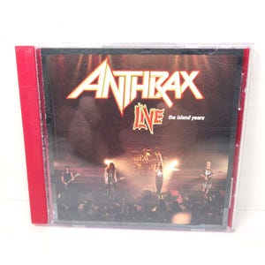 Op de afbeelding: Anthrax Live: The Island Years CD. De CD-hoes heeft een rode rug. De albumhoes toont het logo van de band in wit en rood, met het woord "LIVE" in een gestileerd lettertype. De achtergrond toont de band live op het podium.