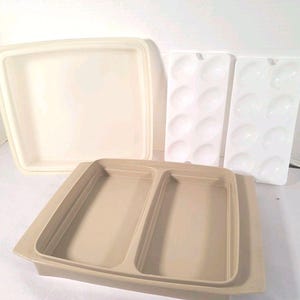 Może przedstawiać: Zestaw beżowych i białych plastikowych pojemników do przechowywania żywności. Zestaw zawiera duży kwadratowy pojemnik z pokrywką, podzieloną prostokątną tacę i dwie tace na jajka. Pojemniki są puste i wyglądają na czyste.