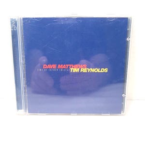 Op de afbeelding: Een cd-hoesje met een blauwe cover. De tekst op de cover luidt "DAVE MATTHEWS LIVE AT LUTHER COLLEGE TIM REYNOLDS" in rood en geel. De hoes is van transparant plastic en heeft een "2 CD"-label.