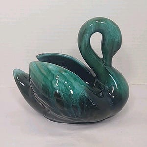 Puede incluir: Un cuenco decorativo con forma de cisne de cerámica en tonos verde y turquesa. El cisne tiene un cuello curvado y alas abiertas que forman un cuenco. El acabado brillante resalta los detalles de las plumas y curvas moldeadas.