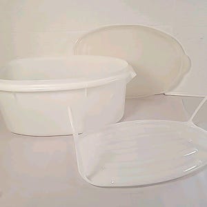 Puede incluir: Un juego de recipientes de plástico blanco para guardar alimentos. El juego incluye un recipiente ovalado grande con tapa y una bandeja ovalada más pequeña con asa. Los artículos son de plástico blanco translúcido.
