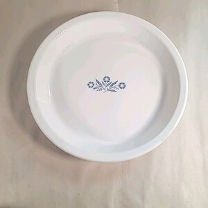 May include: White, round serving plate with a slightly raised edge. The plate features a blue floral design in the center. The plate is likely made of ceramic or a similar material.