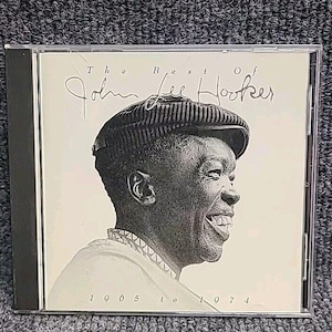 Puede incluir: Una caja de CD con una foto en blanco y negro de John Lee Hooker. El texto en la caja dice "The Best of John Lee Hooker 1965 to 1974".