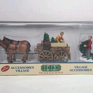 May include: A Lemax Village Collection set featuring a horse-drawn cart with two horses, a figure loading the cart, and a figure holding a wreath. The cart is filled with miniature Christmas trees. The set is packaged in a box with red and white accents.