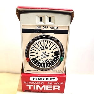 Puede incluir: Un temporizador automático de 24 horas de servicio pesado de color blanco con un dial redondo y marcas negras. El dial tiene las palabras "Día" y "Noche" impresas en él. El temporizador tiene una caja roja y blanca con las palabras "Temporizador automático de 24 horas de servicio pesado" impresas en ella.