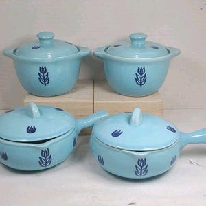 Puede incluir: Cuatro fuentes de cerámica azul claro con tapas. Dos son redondas con asas y dos son redondas con asas pequeñas. Cada una tiene un diseño floral azul oscuro y una tapa a juego con un asa pequeña.