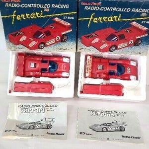 May include: Two vintage Radio Shack Ferrari radio-controlled racing car sets. Each set includes a red toy car, a remote control, and a box with the Ferrari logo and "Radio-Controlled Racing" text. The boxes are blue and red.