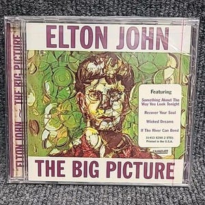 Può includere: Una custodia per CD con un'immagine colorata di Elton John sul davanti. Il titolo "The Big Picture" è stampato in grandi caratteri grassetto. Il CD contiene canzoni come "Something About The Way You Look Tonight", "Recover Your Soul" e "Wicked Dreams".
