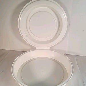 May include: A white, round, plastic container with a matching lid. The lid is open, revealing the interior of the container. The container has a simple, clean design, suitable for food storage or other uses.