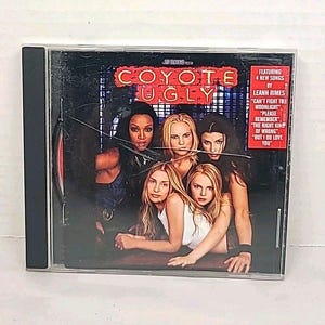 May include: A CD case for the movie "Coyote Ugly" featuring a group of women. The cover has the movie title in red and the names of songs by LeAnn Rimes. The case is in a clear plastic case.