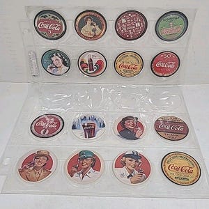 May include: A collection of vintage Coca-Cola bottle caps displayed in a clear plastic sheet. The caps feature various designs, including the Coca-Cola logo, vintage advertisements, and images of women. The caps are round and have a variety of colours.