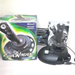 Może przedstawiać: Czarny joystick Microsoft SideWinder Precision 2 z kablem USB, w komplecie z oryginalnym kartonowym opakowaniem i drukowaną instrukcją obsługi. Joystick posiada wyprofilowany uchwyt, srebrny spust oraz okrągłą podstawę.
