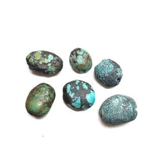 May include: Six irregular, rounded turquoise beads featuring a mix of vibrant blue and green hues with dark brown and black matrix veining. Each bead displays a unique, natural texture and polished surface, showcasing varied patterns of mineral deposits.