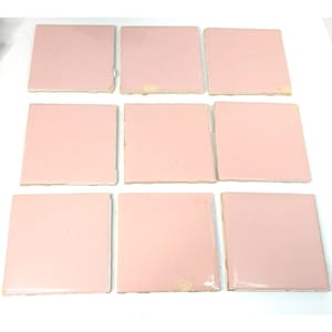 May include: A set of nine square ceramic tiles arranged in a three-by-three grid. Each tile features a smooth, solid light pink glazed finish with straight edges and corners. The tiles are uniform in shape and color, displaying a glossy surface.