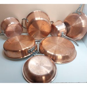 May include: A collection of seven copper cookware pieces, including various pots and pans with metallic handles. The underside of one pan features the stamped text "Copral Made in Portugal" and "1368 8". The copper surfaces show a polished finish.