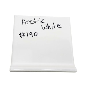 Könnte beinhalten: Eine weiße Keramikfliese mit den Worten "Arctic White" und der Nummer "#190" in schwarzem Marker geschrieben. Die Fliese hat eine gebogene Kante an der Unterseite.