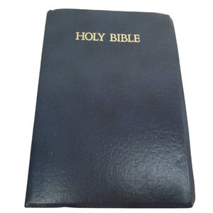 May include: A navy blue Holy Bible with gold lettering. The book has a textured cover and is closed. The title "HOLY BIBLE" is prominently displayed on the front cover.