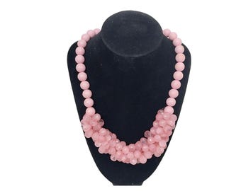 May include: A pink beaded necklace with a layered design. The necklace is displayed on a black velvet stand.