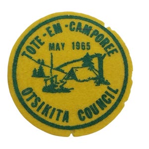 Może przedstawiać: Okrągła naszywka w kolorze żółtym i zielonym z napisem "Tote-Em-Camporee May 1965 Otsikita Council" w kółku.