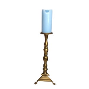 May include: A tall, ornate gold-colored candlestick with a light blue candle. The candlestick has a decorative base and a slender, detailed stem. The candle is cylindrical and has a slightly melted appearance.