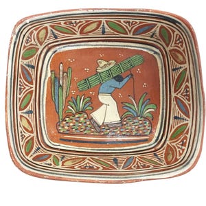 May include: Square, hand-painted ceramic plate with a terracotta background and a border of green, blue, and red designs. The central image depicts a person carrying a bundle, surrounded by cacti and plants. The plate measures approximately 10 inches square.