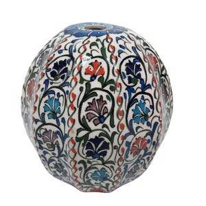 May include: A ceramic decorative sphere with a white base, adorned with a vibrant floral pattern in shades of blue, red, green, and purple. The design features intricate swirling vines and stylized flowers, creating a detailed and colorful aesthetic. The sphere has a small opening at the top.