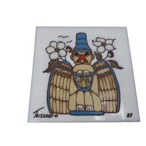 May include: Square ceramic tile with a Native American-inspired design. The artwork features a central figure with a bird-like face, wings, and a blue headdress. White flowers and birds are also depicted. The tile is signed "Teissedre" and numbered "85".
