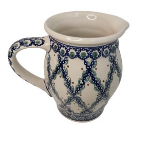 May include: A white ceramic pitcher with a handle and spout. The pitcher is decorated with a blue and green lattice pattern and small red dots. The handle and rim have a matching blue and green design. This pitcher is ideal for serving beverages.