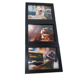 May include: A black triple picture frame with three images of Muppet characters. The top image shows a Muppet puppet near a parking meter. The middle image shows a Muppet puppet with its hands over its eyes. The bottom image shows a Muppet puppet playing a piano.