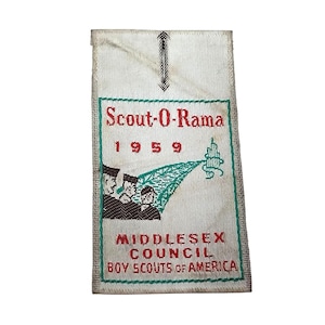 May include: A rectangular, off-white fabric patch with green and red text and graphics. The patch reads "Scout-O-Rama 1959" and "Middlesex Council Boy Scouts of America." The patch features an illustration of three figures and a stylized tree.