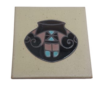 May include: A square ceramic tile with a beige speckled background. The tile features a stylized design of a dark brown pot with black, pink, and turquoise accents. The design is centered on the tile.